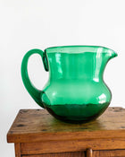 Green glass pitcher on a wooden surface with a white background