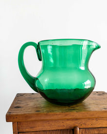Green glass pitcher on a wooden surface with a white background