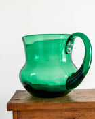 Green glass pitcher with handle on a wooden surface
