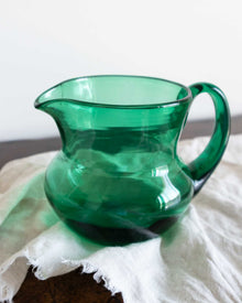 Green glass pitcher on a white surface with a blurred background
