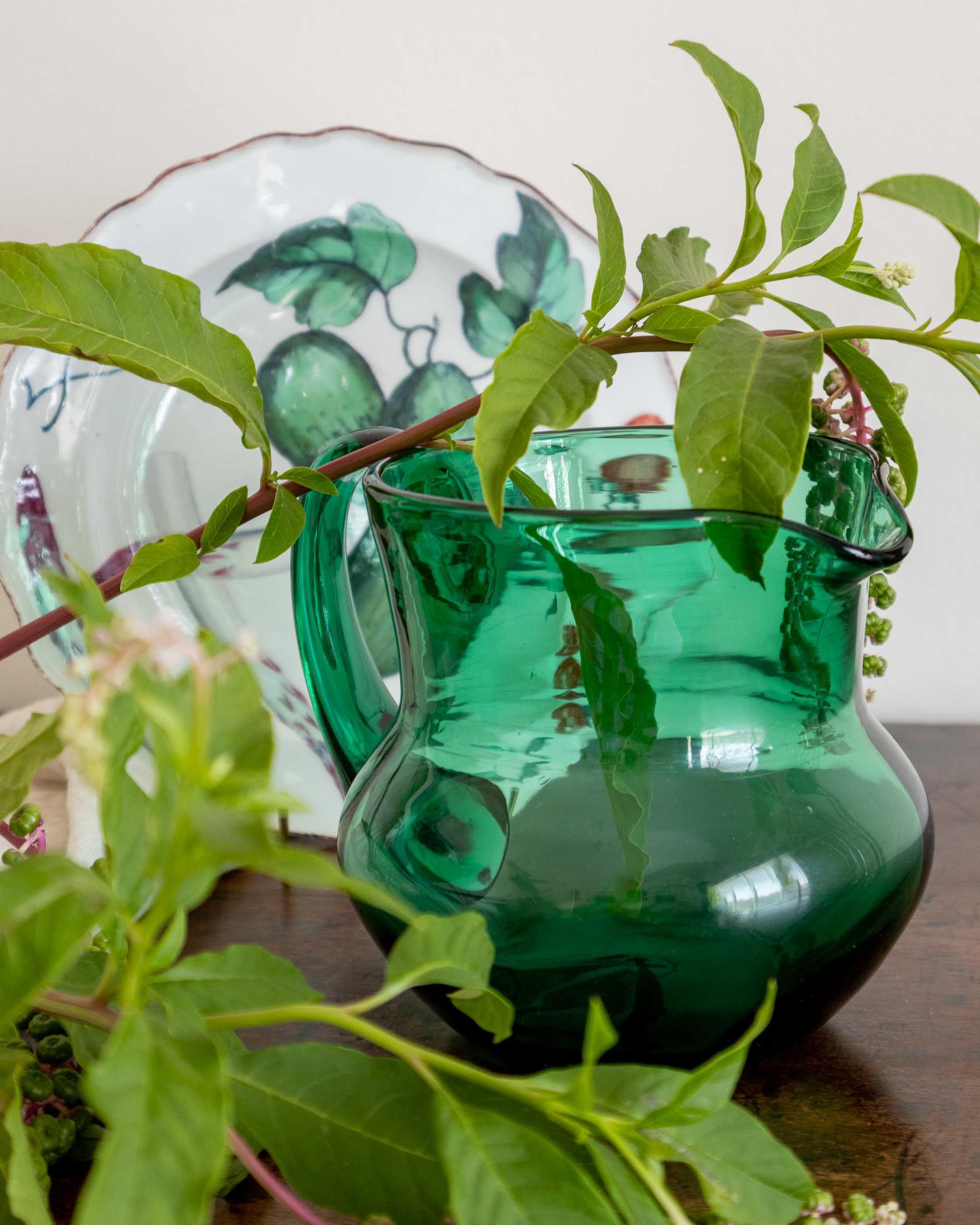 Green glass pitcher with leaves on a wooden surface
