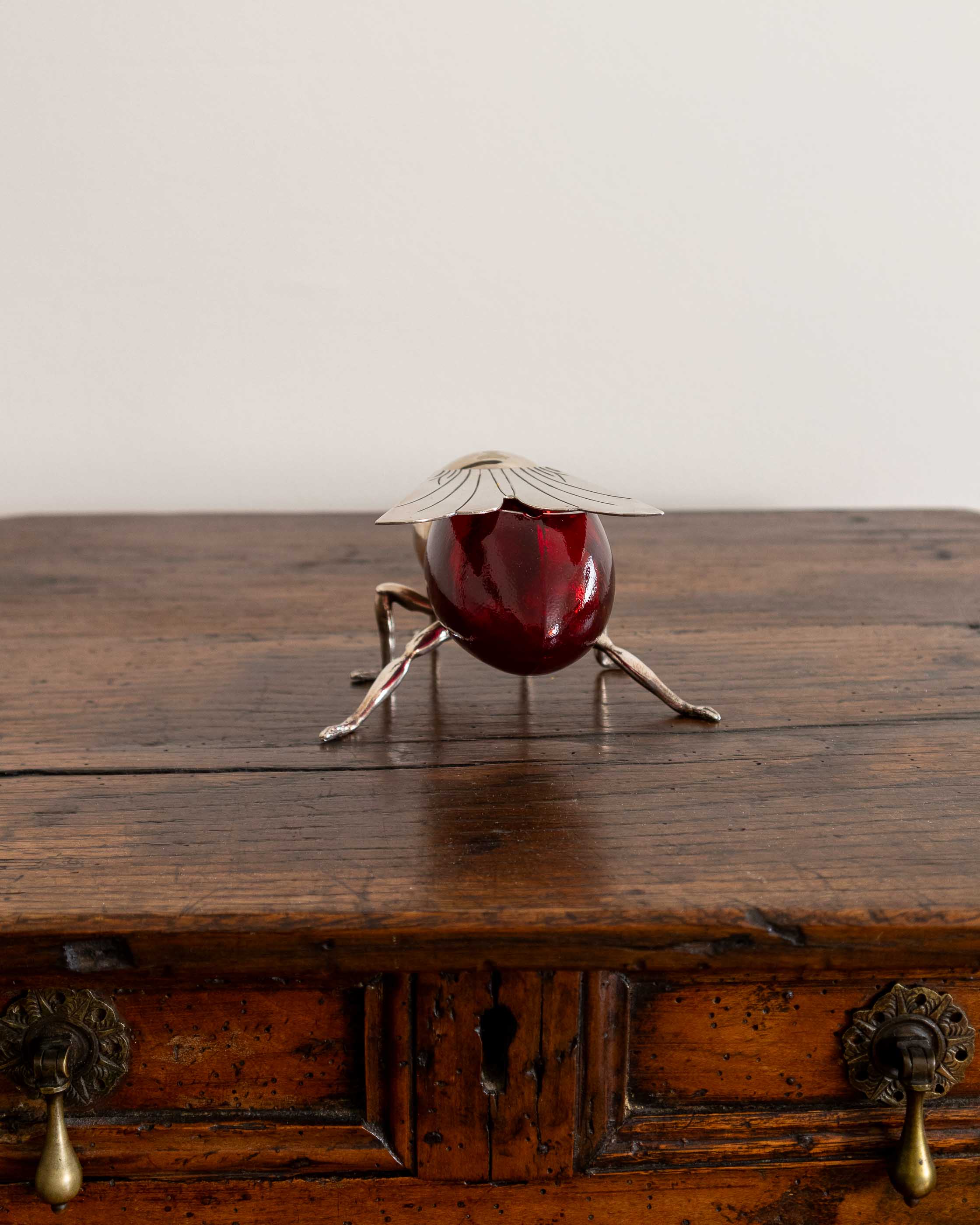 Decorative bee honey pot with a red glass base and metal legs on a wooden surface