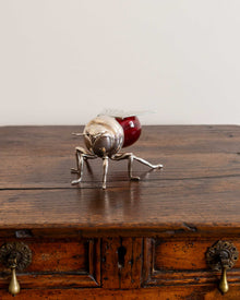 Decorative object resembling a silver bee with a red body on a wooden surface