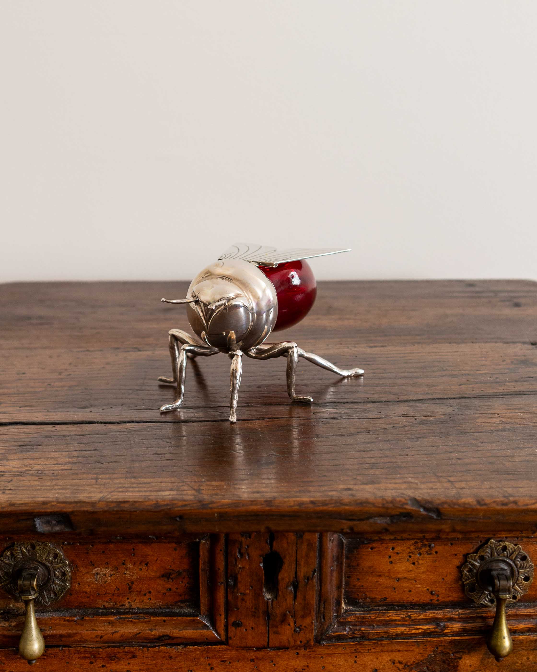 Decorative object resembling a silver bee with a red body on a wooden surface