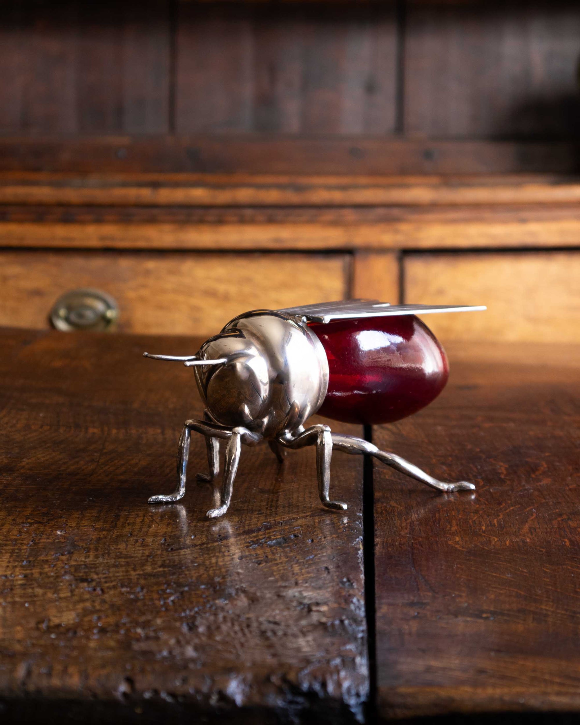 Decorative bee honey pot with a red glass base and metal legs on a wooden surface