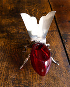Decorative bee honey pot with a red glass base and metal legs on a wooden surface
