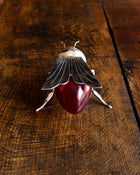Decorative bee honey pot with a red glass base and metal legs on a wooden surface