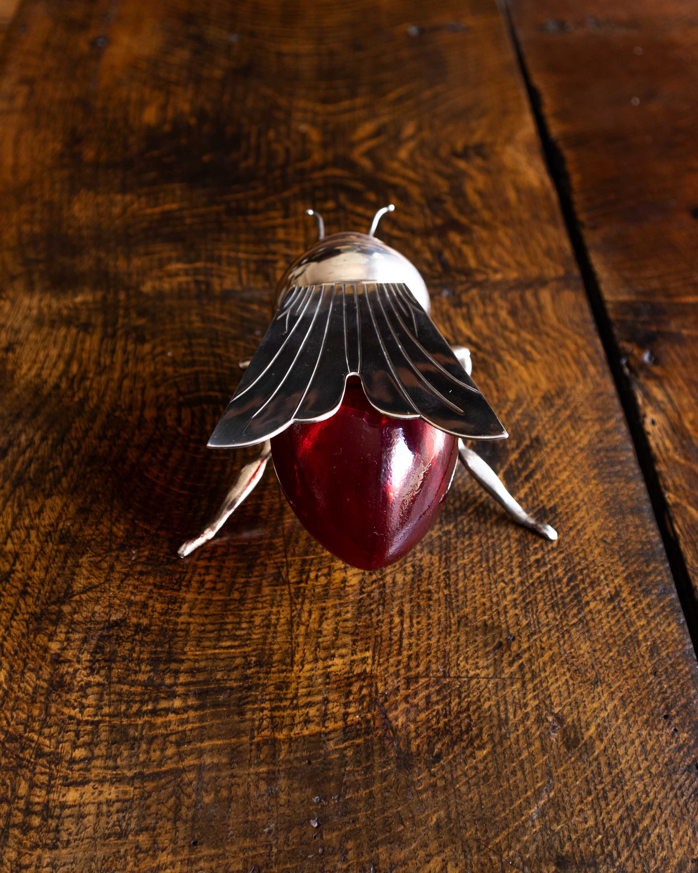 Decorative bee honey pot with a red glass base and metal legs on a wooden surface