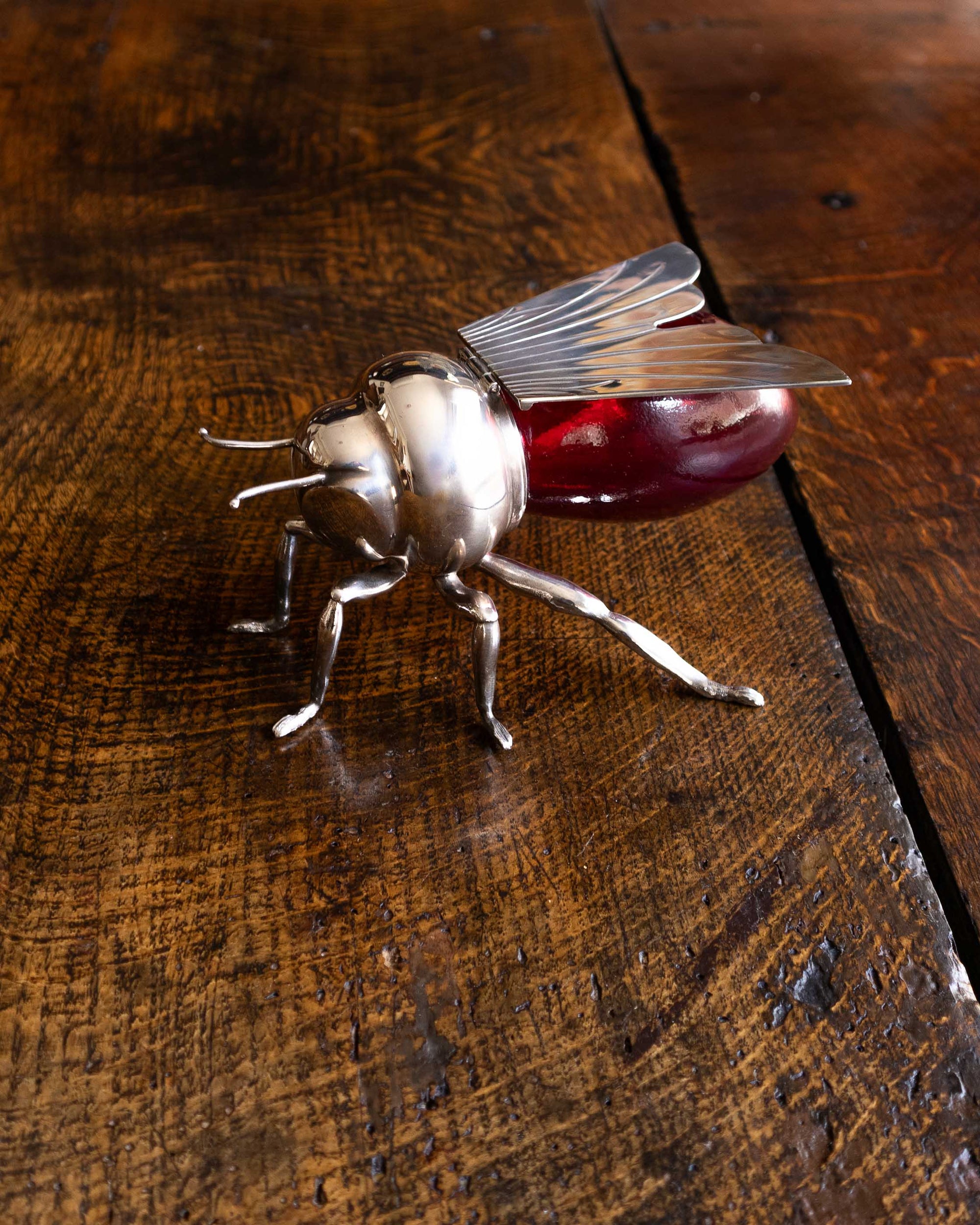 Decorative bee honey pot with a red glass base and metal legs on a wooden surface