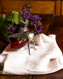 Decorative bee honey pot with a red glass base and metal legs on a wooden surface with flowers in the background