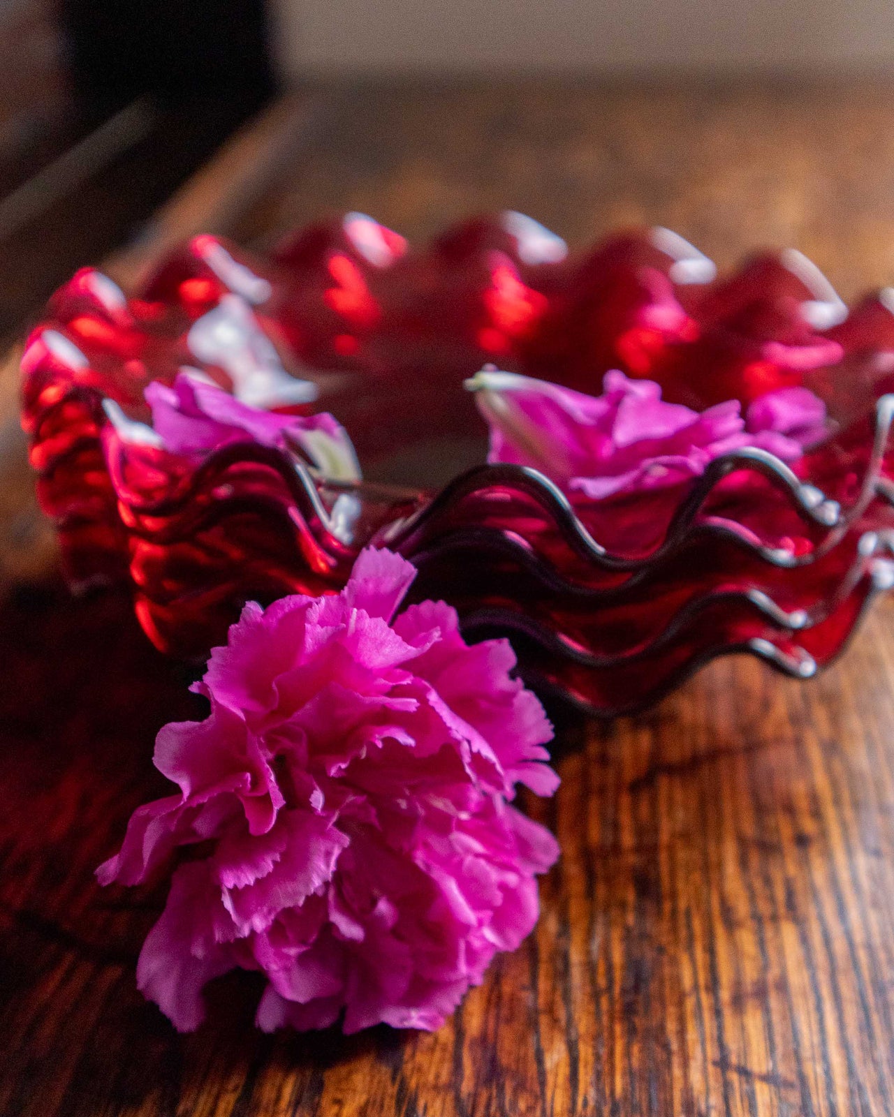 Red wavy glass bowl with a pink flower on a wooden surface