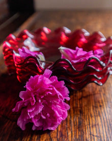 Red wavy glass bowl with a pink flower on a wooden surface