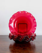 Pink glass bowl with wavy rim on a wooden surface