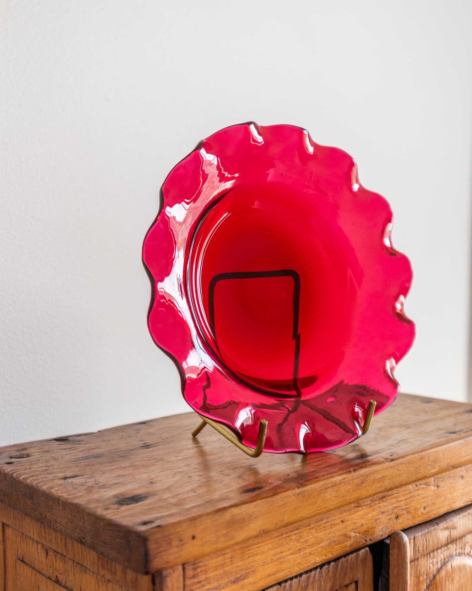 Red glass plate with scalloped edge on a wooden stand against a white background