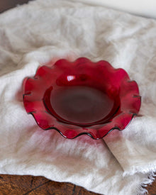Red glass bowl with wavy edge on a white fabric background
