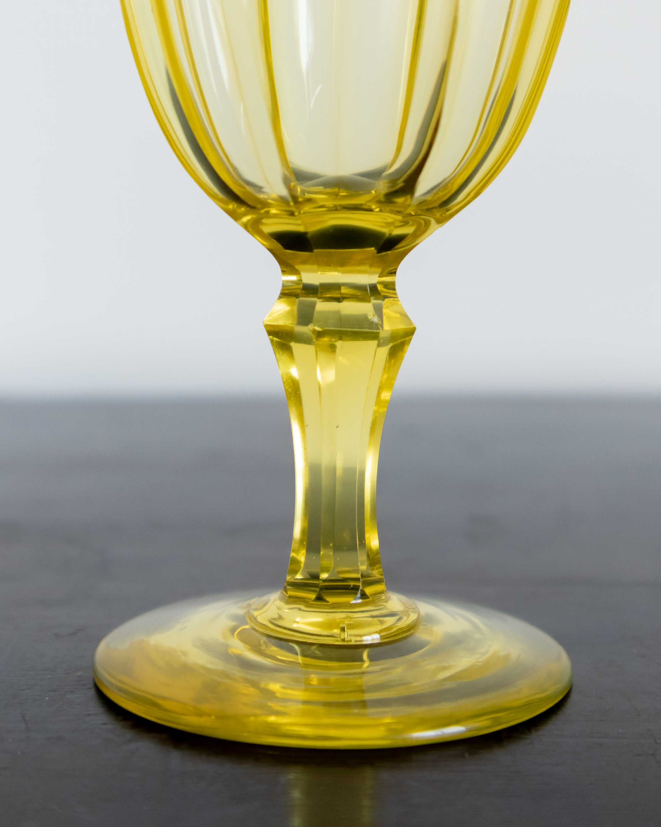 Yellow glass goblet on a dark surface with a light gray background