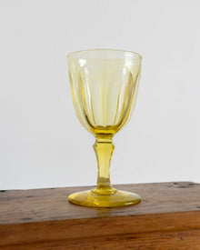 Yellow glass goblet on a wooden surface with a white background