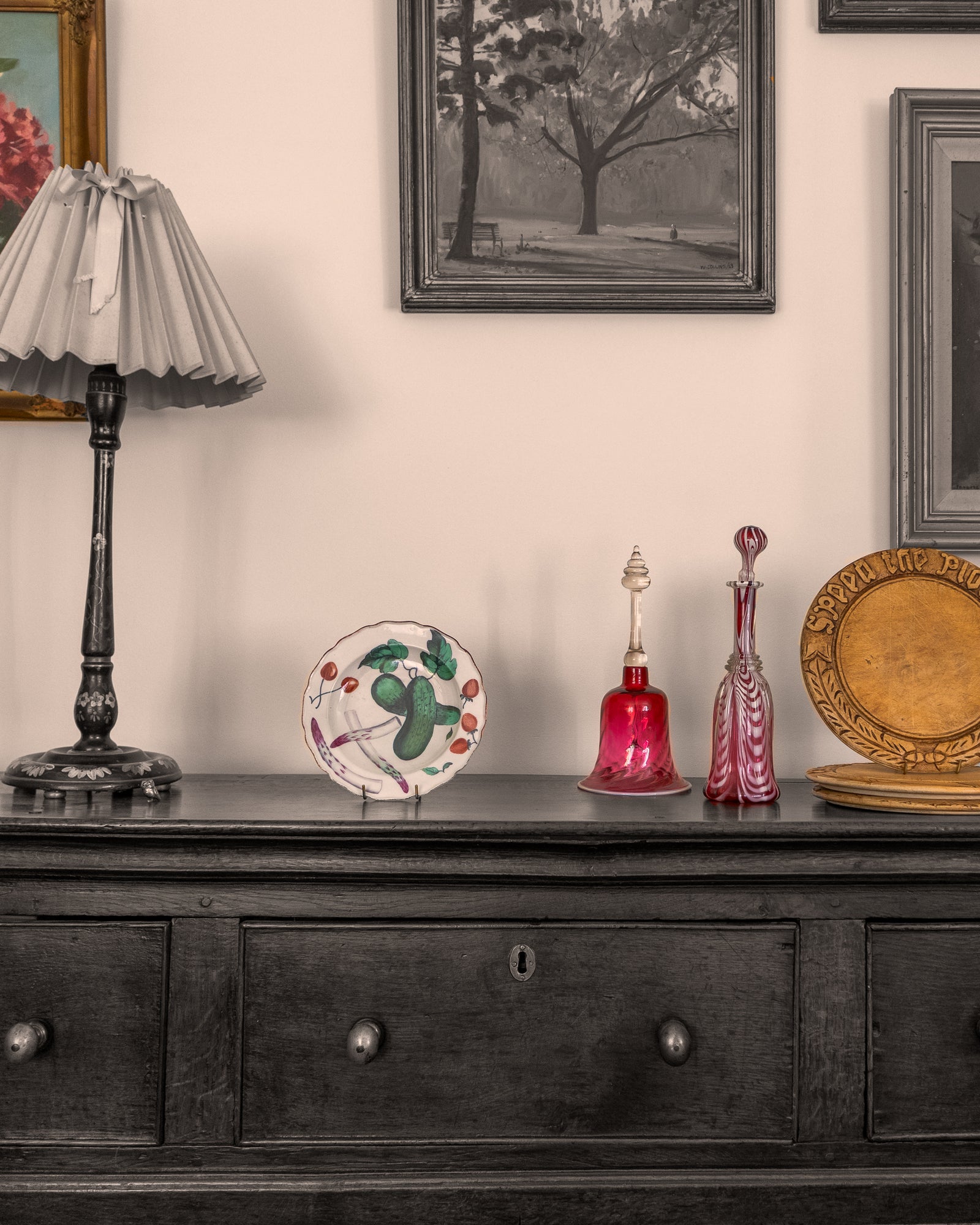 Antique Georgian dresser with decorative items including a lamp, Chelsea porcelain plate, and Nailsea glass decanters against a wall with framed artwork.