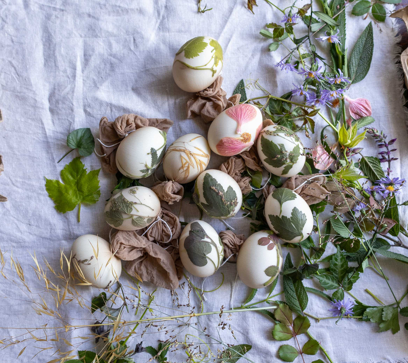 Decorative eggs with leaf patterns on a white fabric background with flowers and leaves.