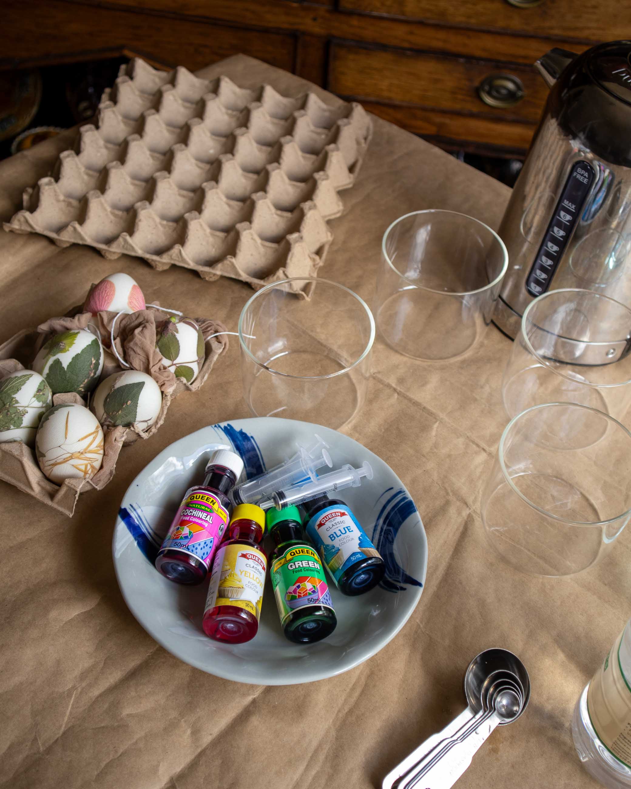 Decorative eggs, dye and glass jars on a brown paper table.