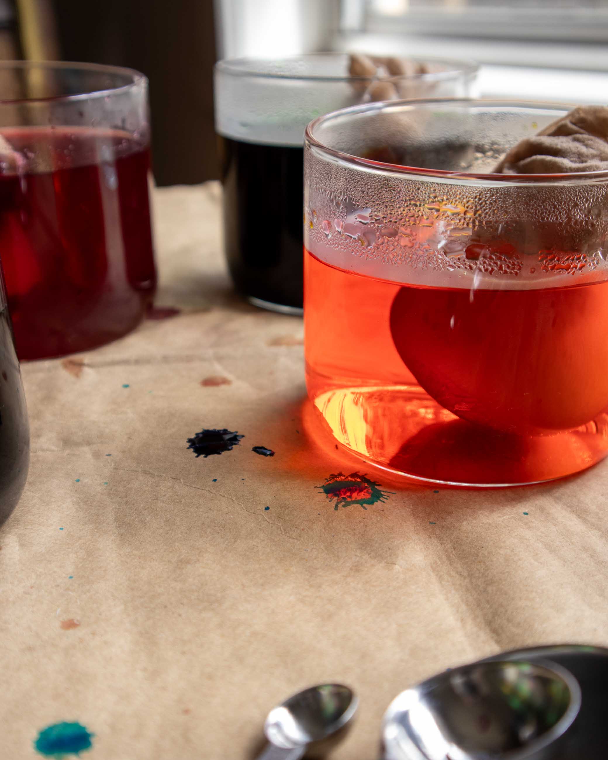 Red liquid dye in a glass on a textured surface with a spoon and other items in the background.