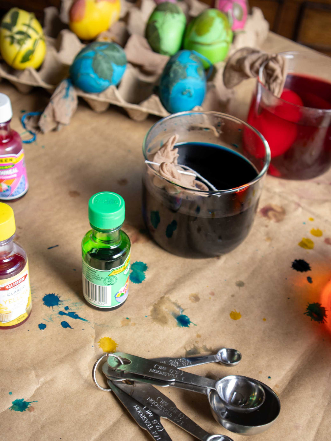 Easter egg dyeing setup with bottles, a glass of dark liquid, and colorful eggs on a brown paper background.