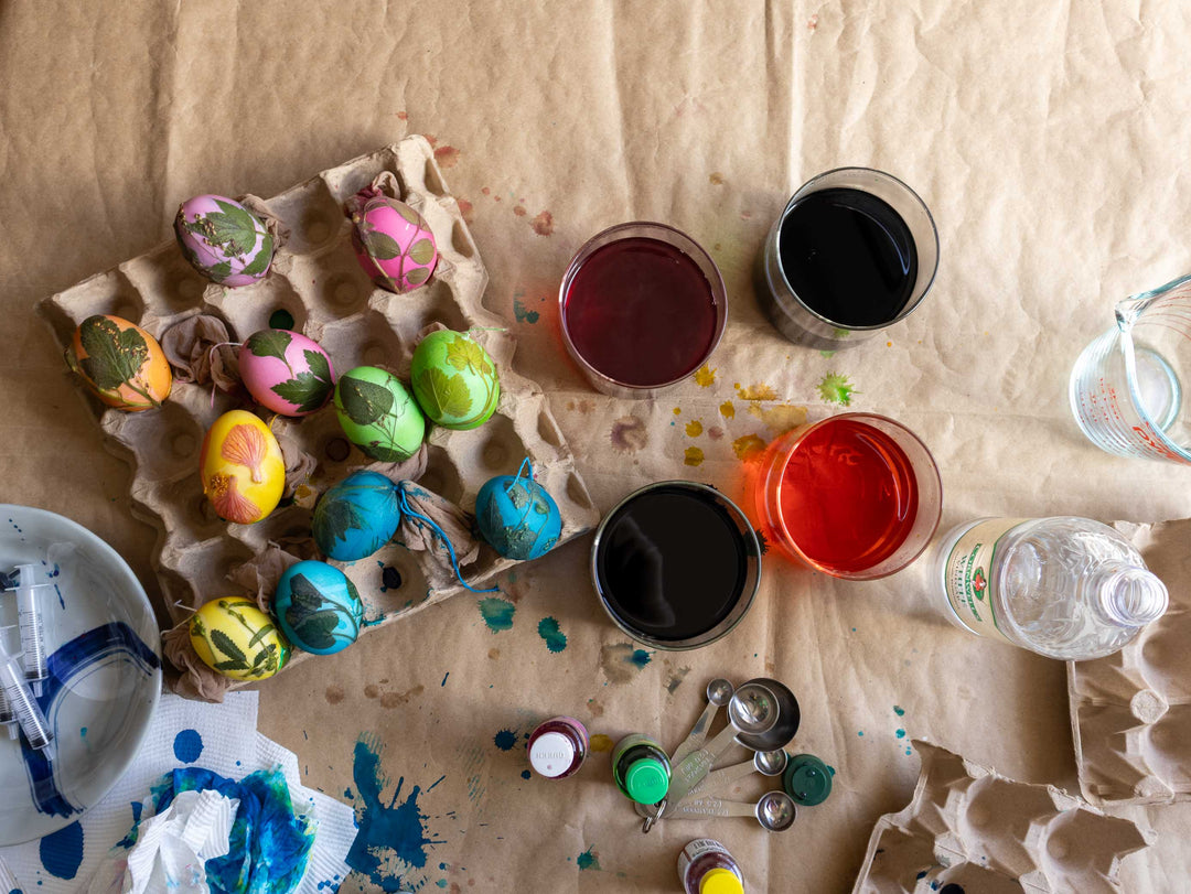 Easter egg dyeing setup with colored eggs, bottles, and containers on a table.