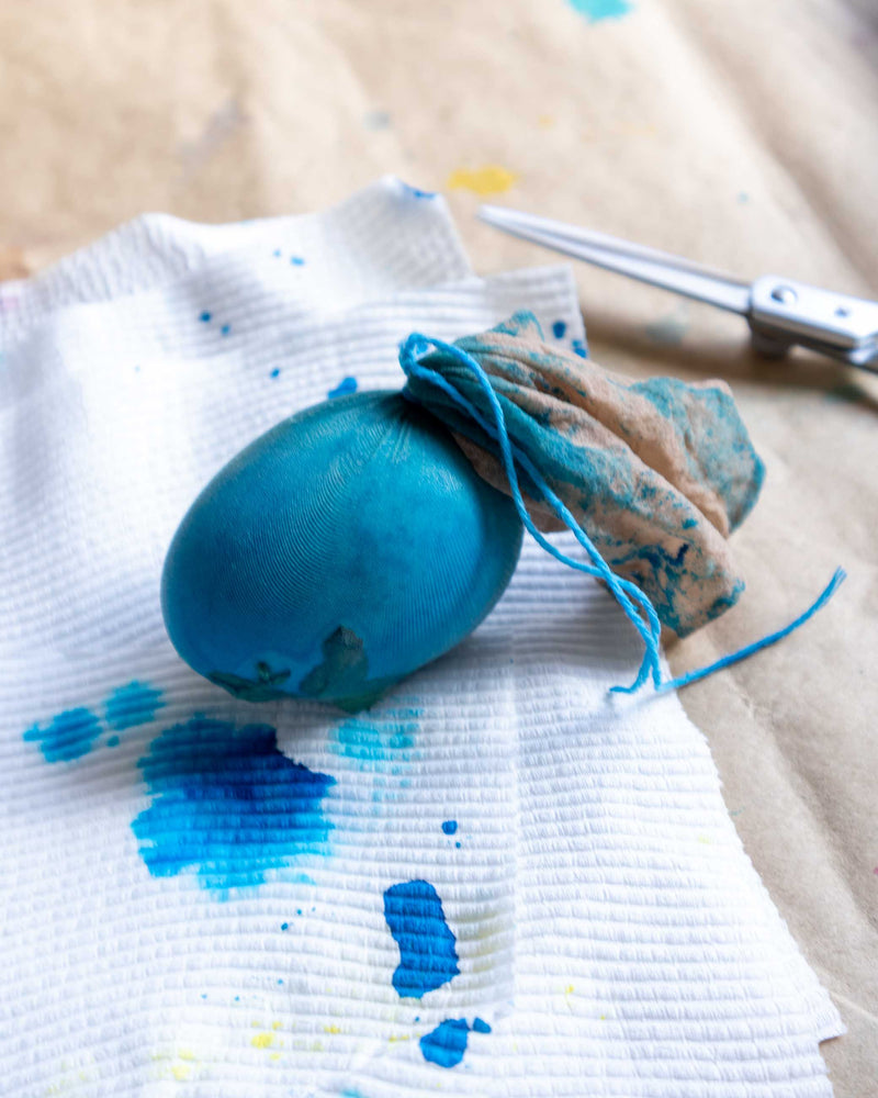 Blue egg with string, scissors, and paint splashes on a textured surface