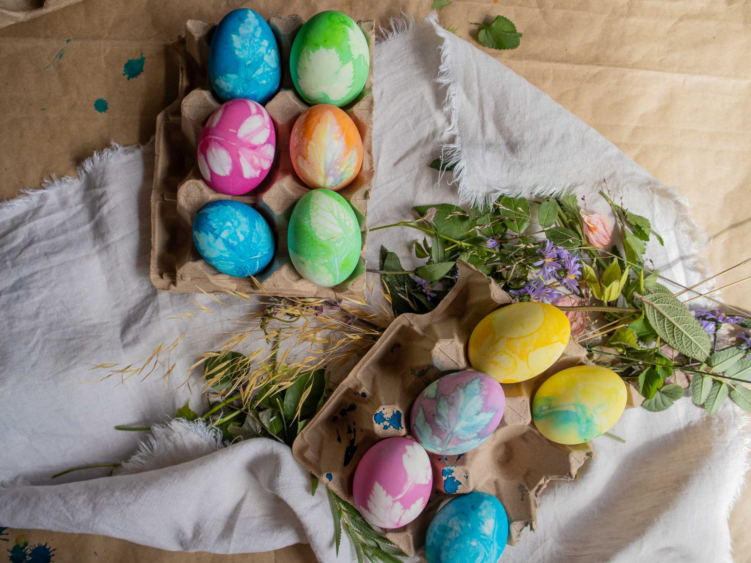 Colorful Easter eggs in a cardboard carton with flowers on a rustic background