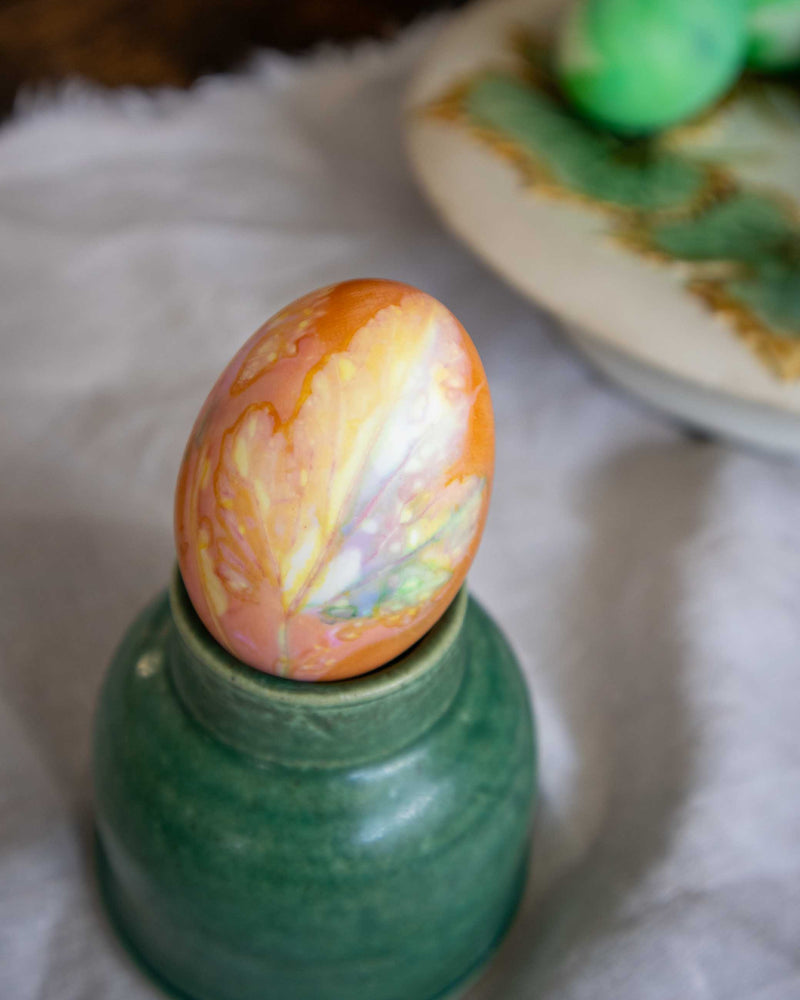 Decorative egg with marbled pattern on a green stand against a white background