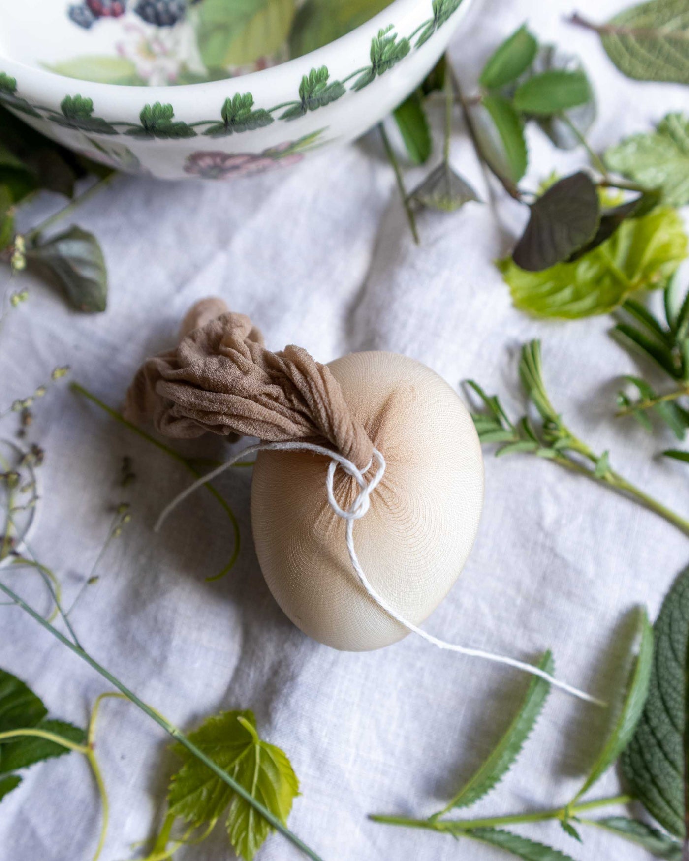 Egg wrapped with panty hose tied with string on a white cloth with green leaves