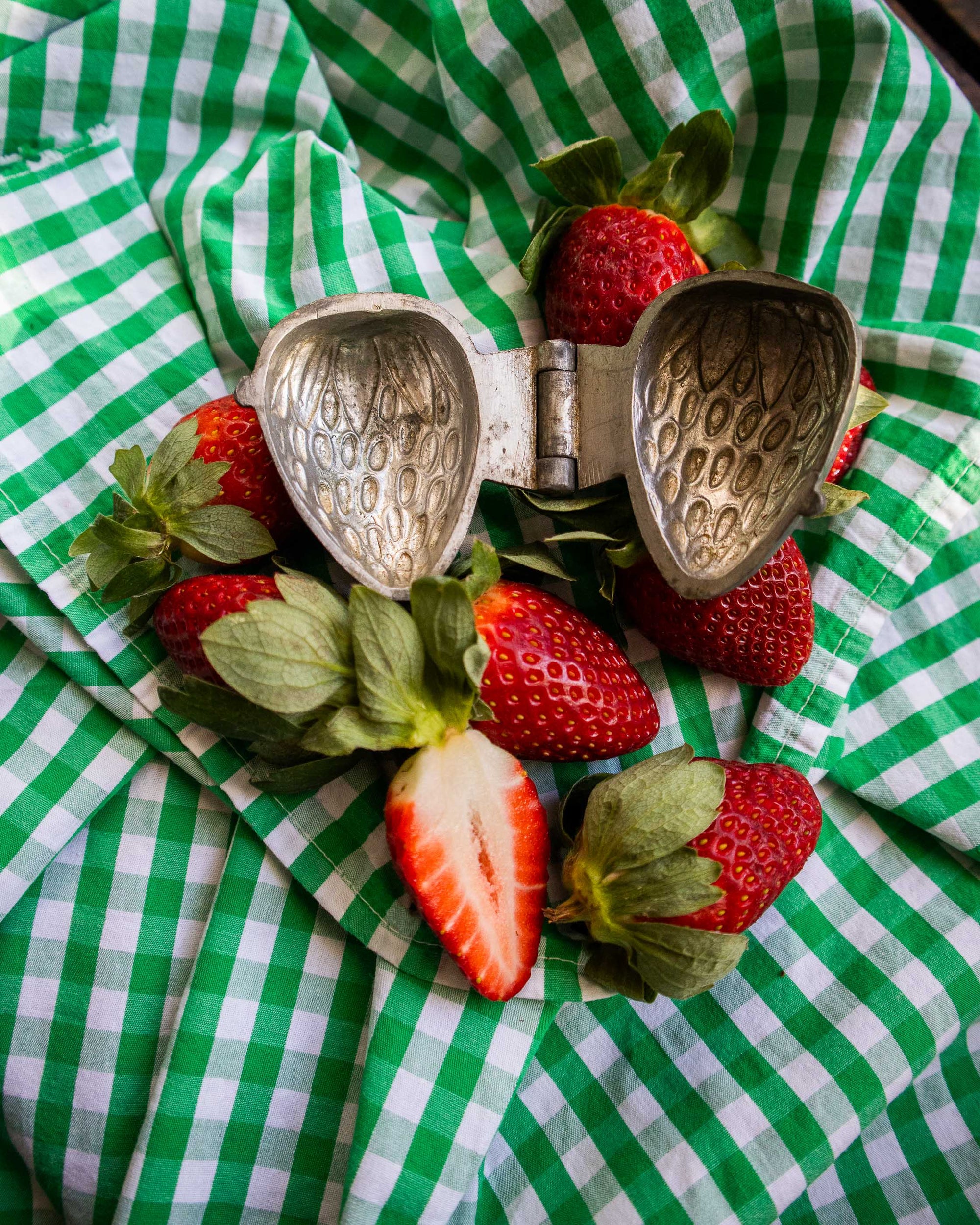 Strawberry pewter mould surrounded by strawberries on a green and white checkered cloth