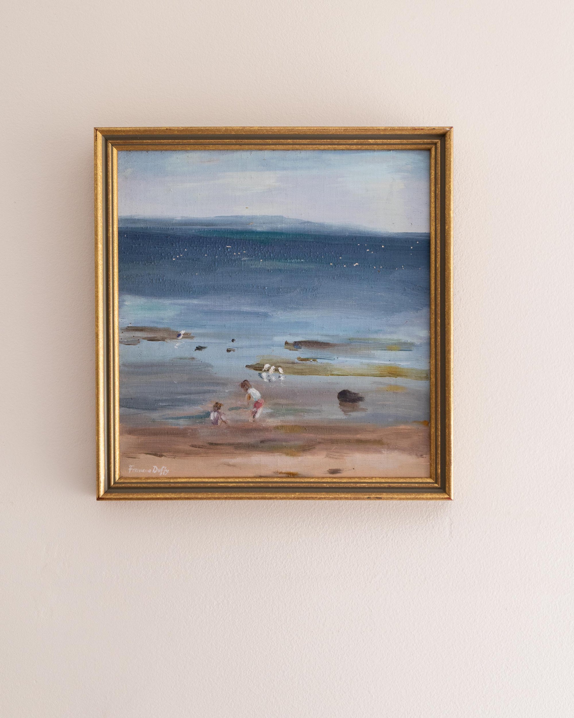 Framed painting of a beach scene with people on a light beige wall