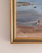 Framed painting of a beach scene with a signature on a beige wall