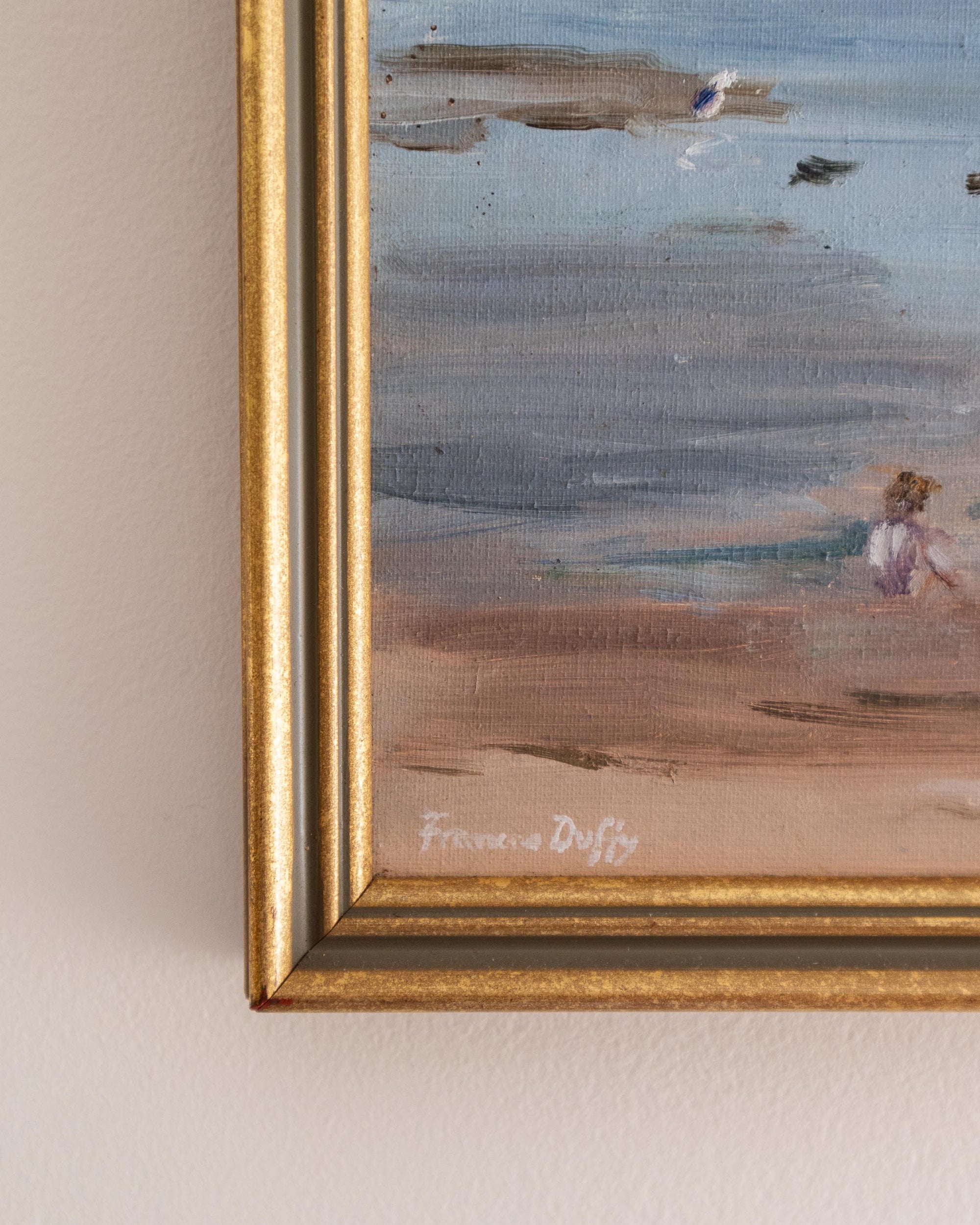 Framed painting of a beach scene with a signature on a beige wall