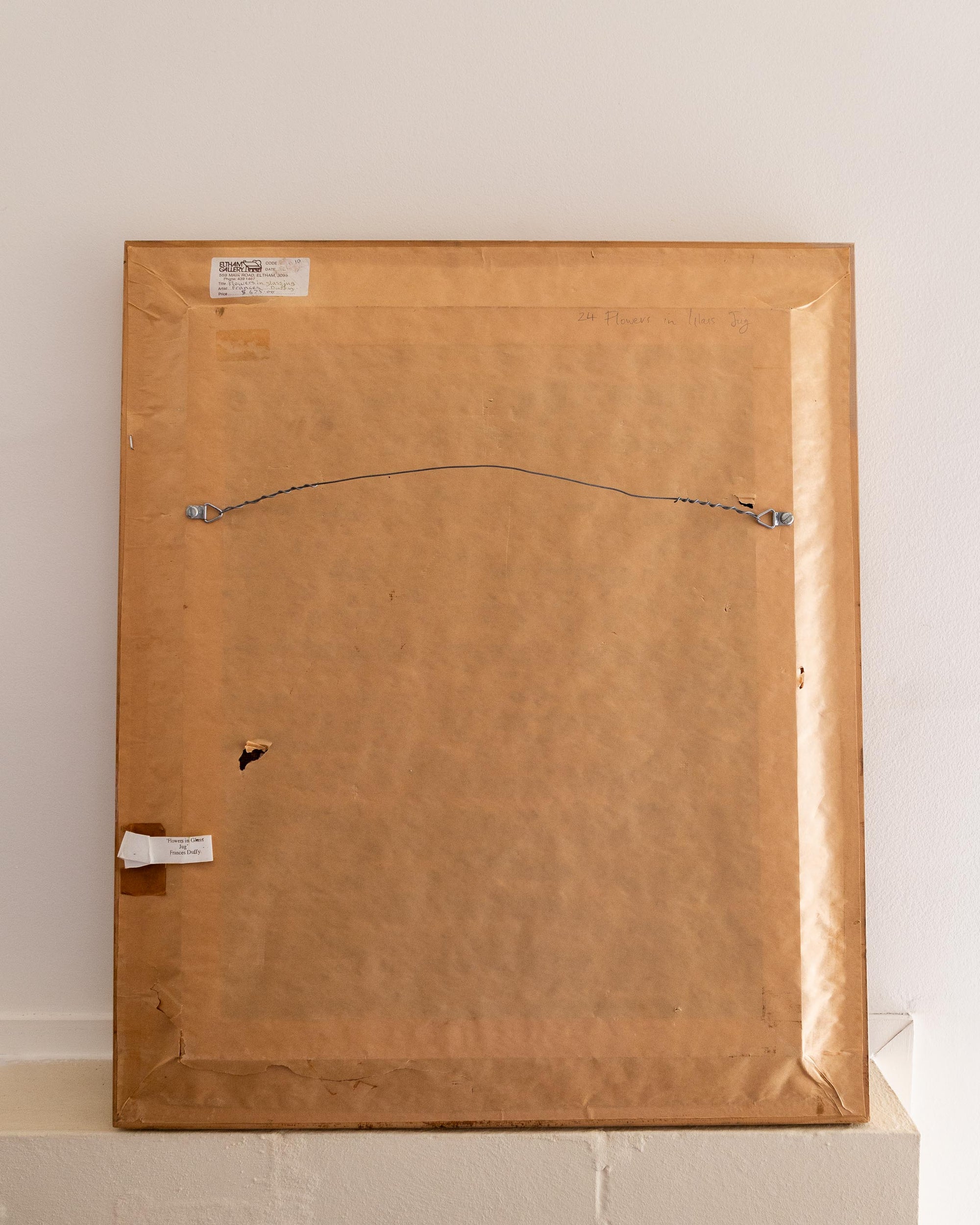 Back of a painting with visible hardware and labels on a white surface