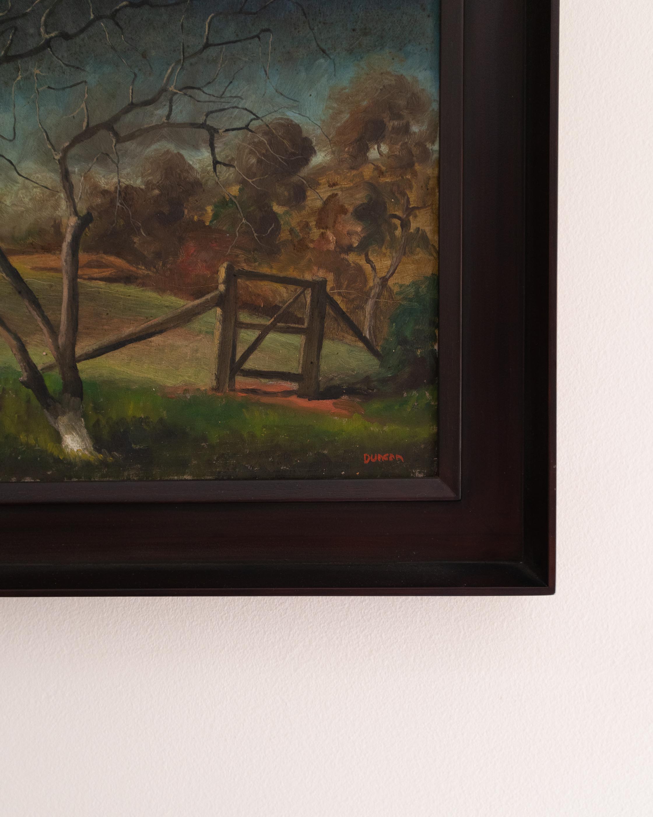 Framed painting of a landscape with a gate and trees on a wall.