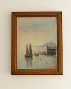 Framed painting of a harbor scene with sailboats and a wooden building.
