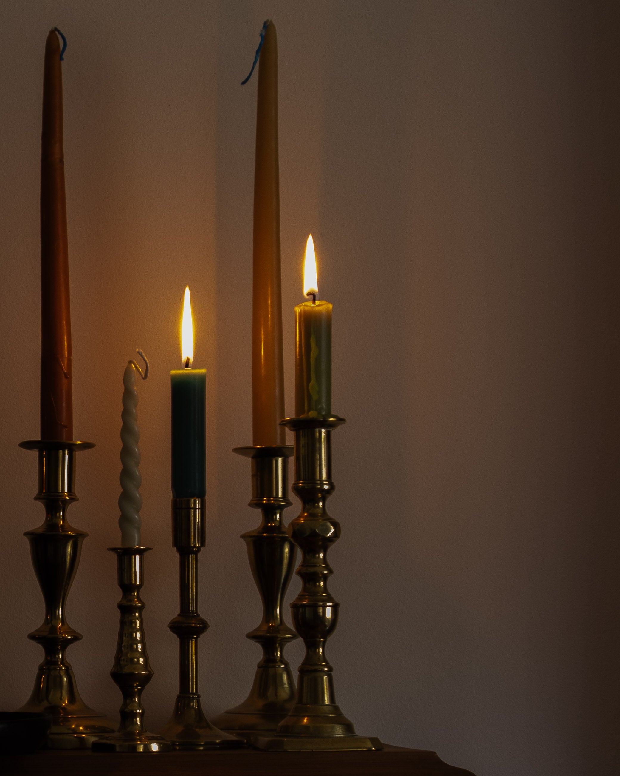 Group of lit candles in brass candlesticks against a plain background