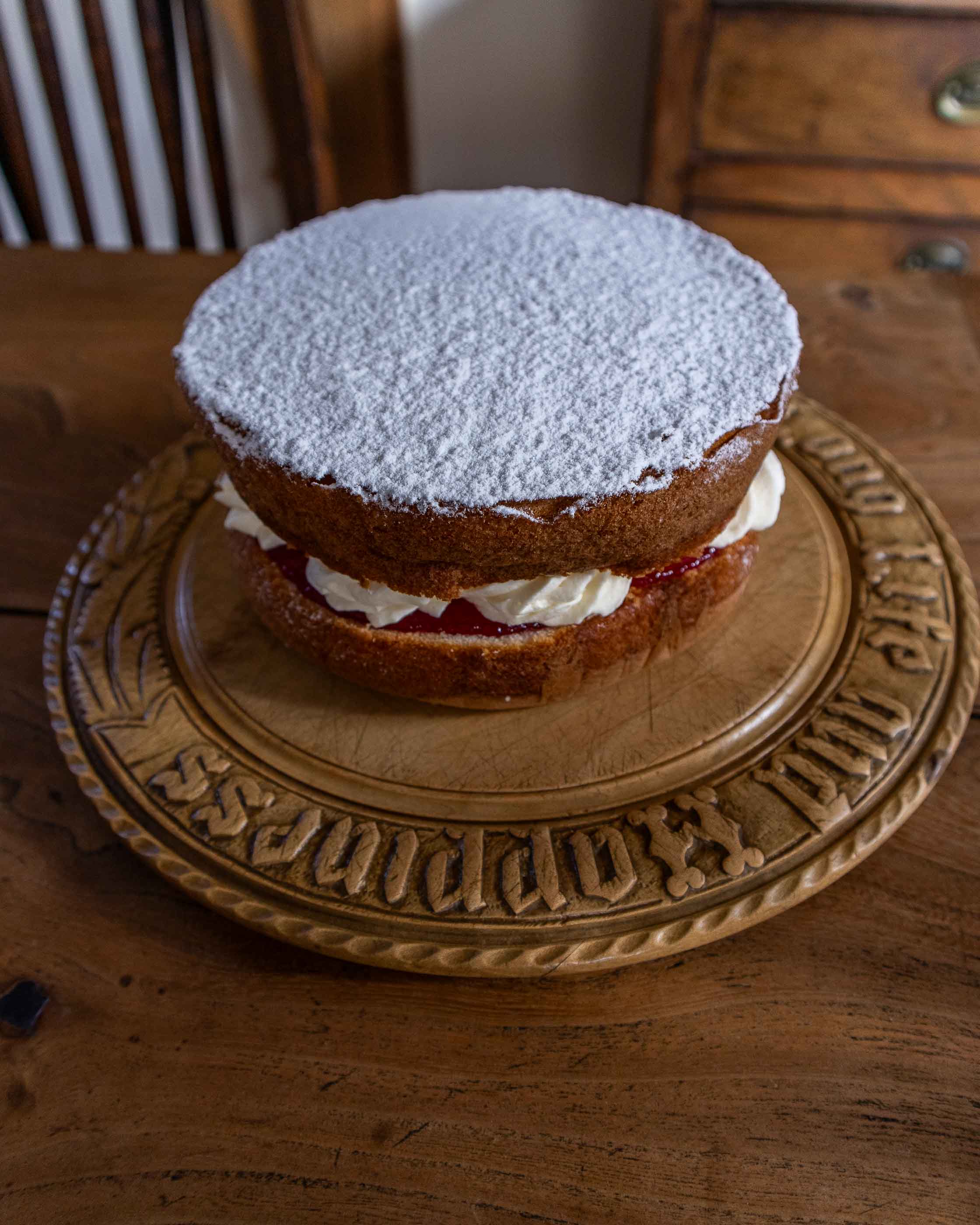 Two-layered cake with white frosting and jam on a decorative wooden breadboard.
