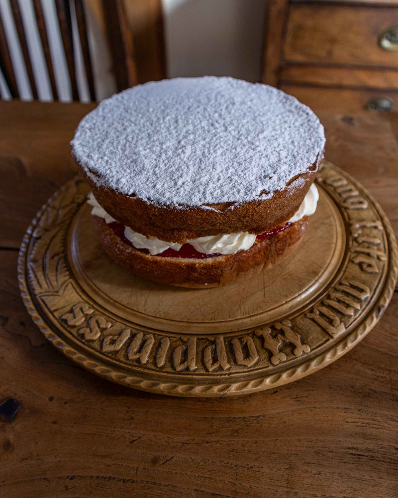 Two-layered cake with white frosting and jam on a decorative wooden breadboard.