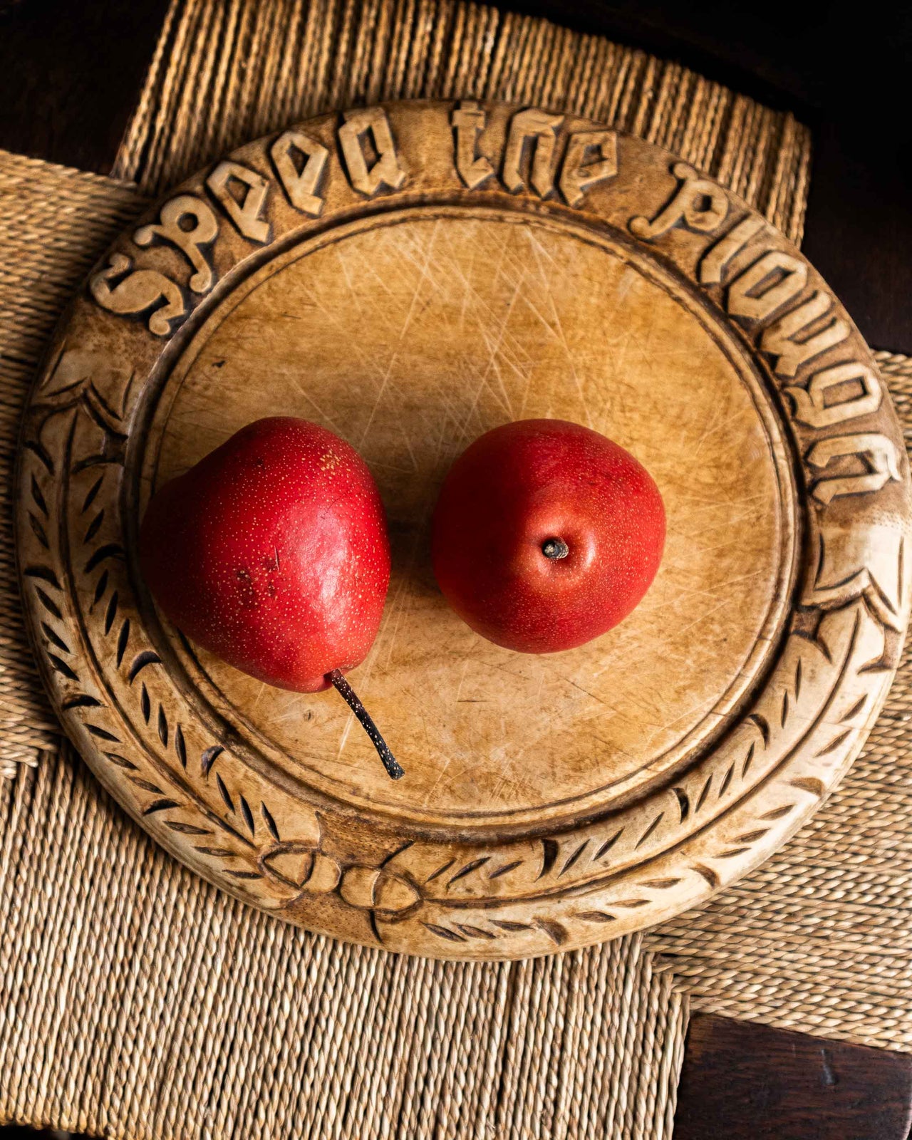 Two red pears on a decorative wooden breadboard with carved text.