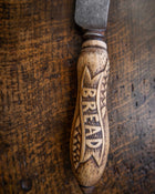 Wooden bread knife handle engraved with 'BREAD' on a wooden surface