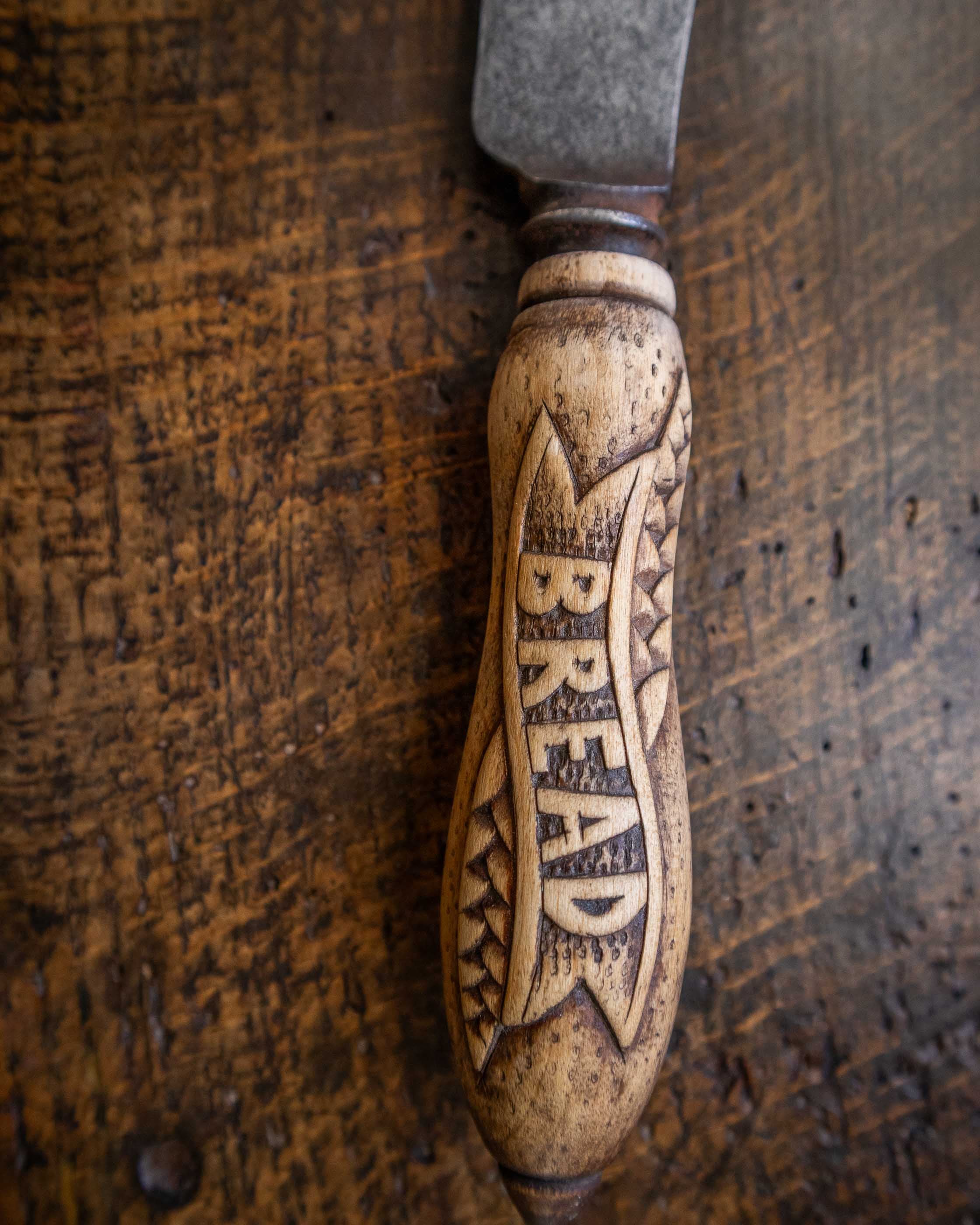 Wooden bread knife handle engraved with 'BREAD' on a wooden surface