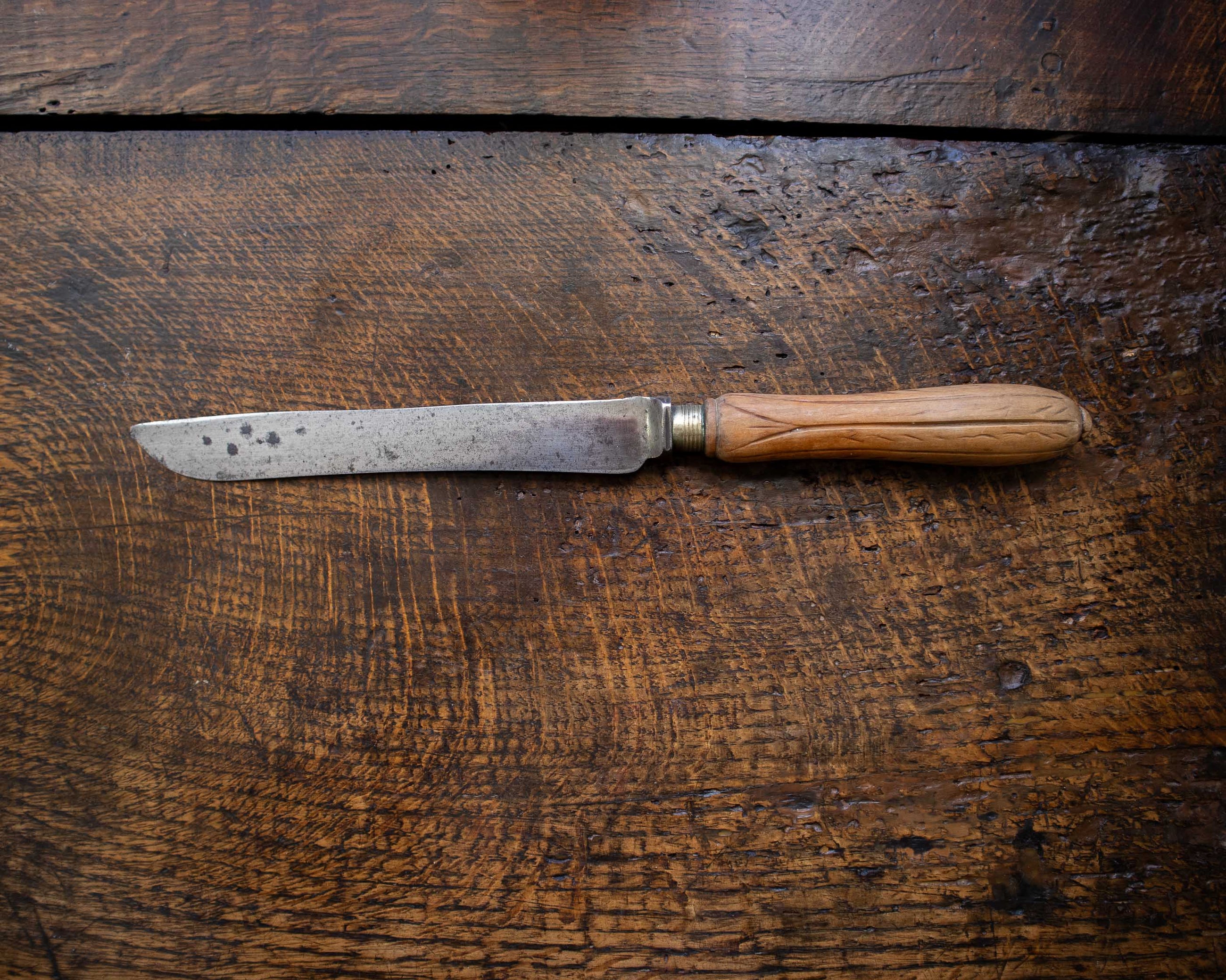 Old bread knife with a wooden handle on a rustic wooden surface