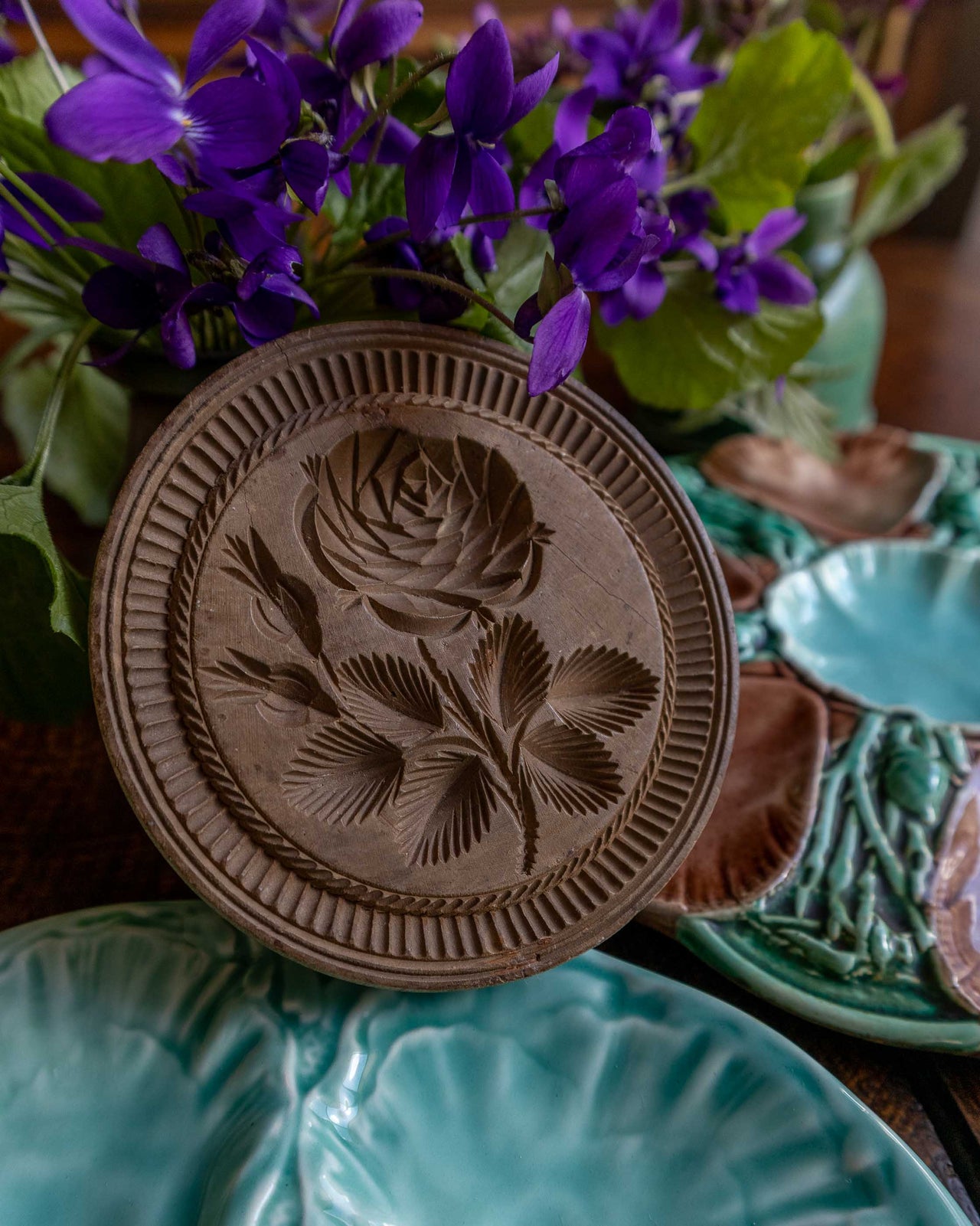 Wooden butter stamp with floral design on a table with flowers and ceramic plates.