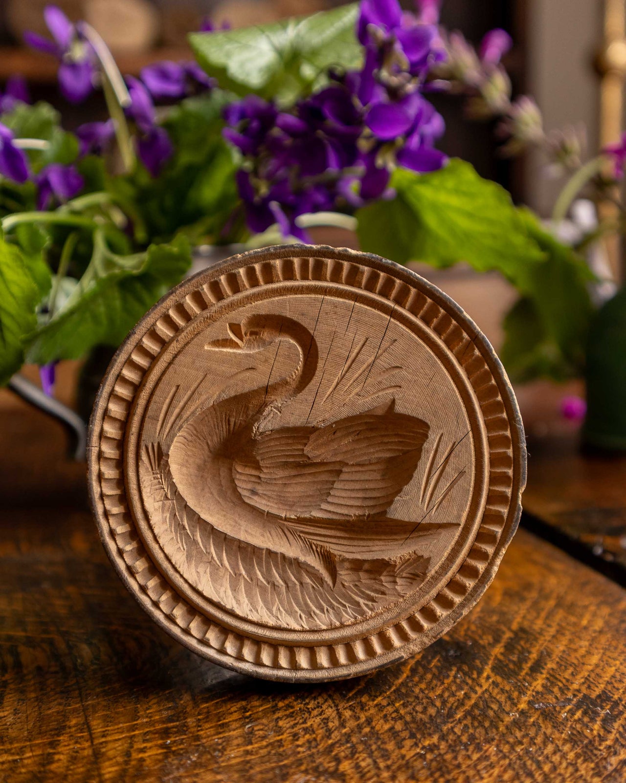 Wooden butter stamp with a swan design on a wooden surface with flowers in the background