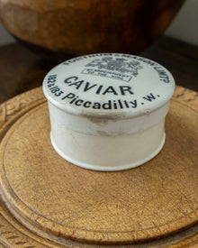 Vintage-style caviar container with a decorative lid on a wooden surface