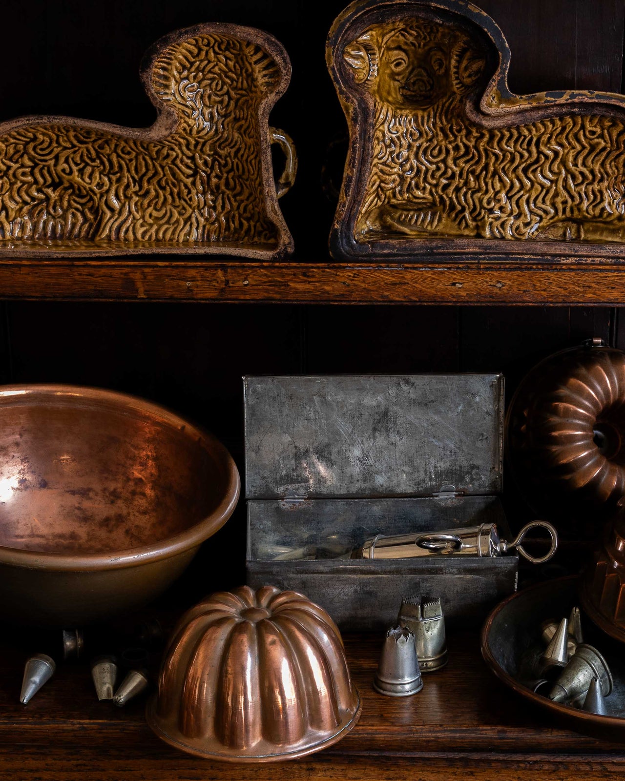 Collection of vintage metal kitchen utensils including cake moulds and a copper bowl on a wooden surface.