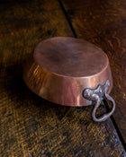 Copper dish with a handle on a wooden surface